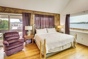 A bedroom with a large bed, a chair, and a view of a body of water.
