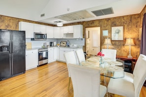 A modern kitchen with white cabinets, a black refrigerator, a microwave, and an oven. There is a dining table with white chairs and a glass top.