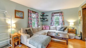 A cozy living room with a sectional sofa, a coffee table, and a side table with a lamp. There are floral curtains on the windows, and a painting on the wall. - 1 Mi to Dtwn Binghamton: Pet-friendly Home w/ Deck (Binghamton)