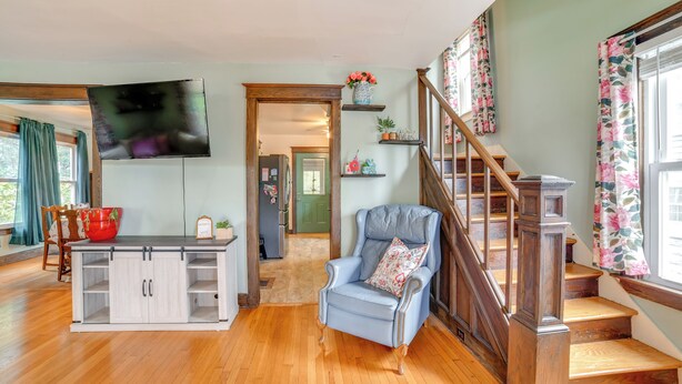 A spacious living room with a wooden staircase, a large flat-screen TV mounted on the wall, and a dining area with a wooden table and chairs. - 1 Mi to Dtwn Binghamton: Pet-friendly Home w/ Deck (Binghamton)