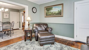 A room with a brown leather armchair, a dining table with chairs, a clock, and a framed landscape painting on the wall. - 2 Mi to Mohegan Sun & Dtwn: Home in Norwich (Norwich)