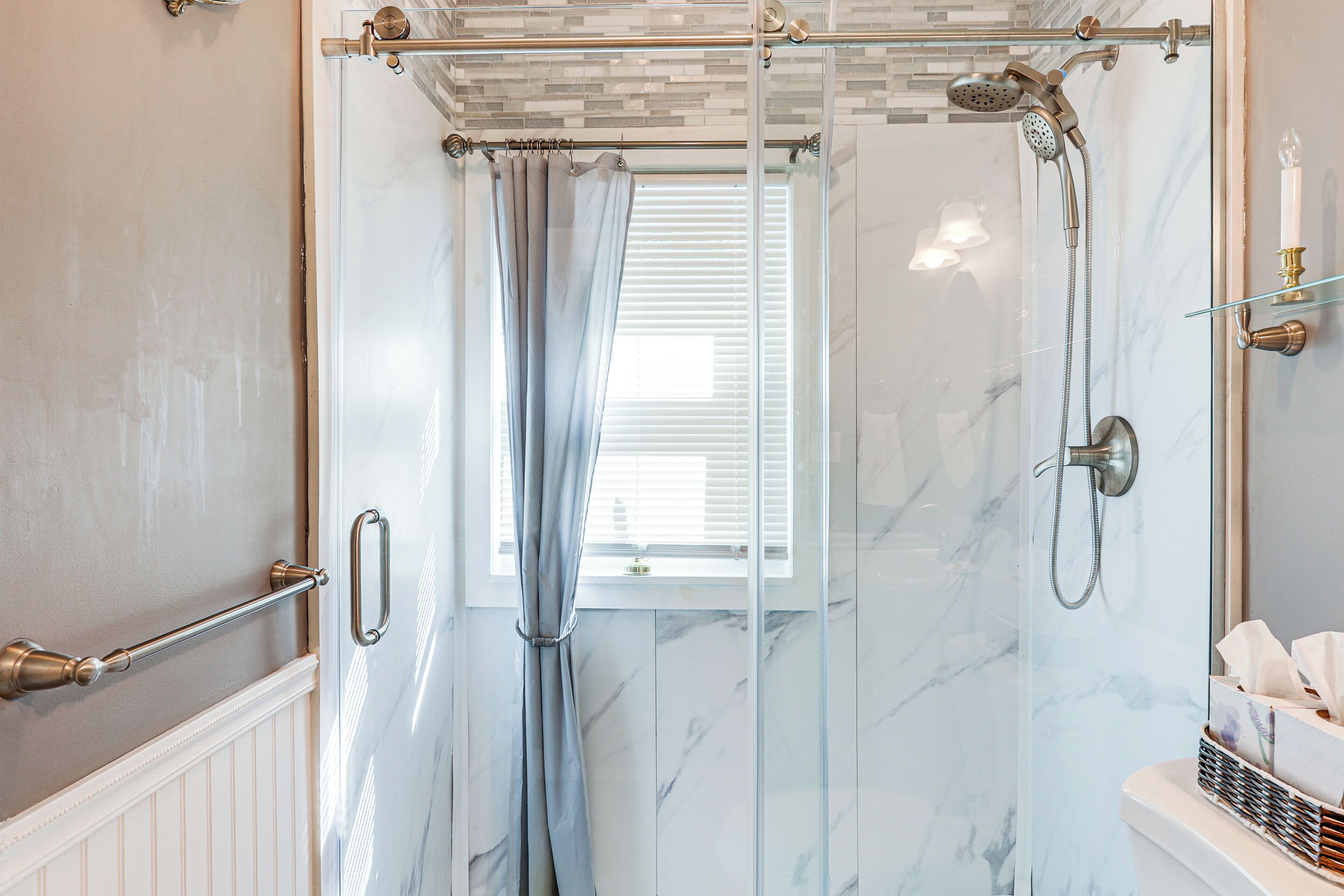 A glass-enclosed shower with a handheld showerhead and a handheld shower attachment.