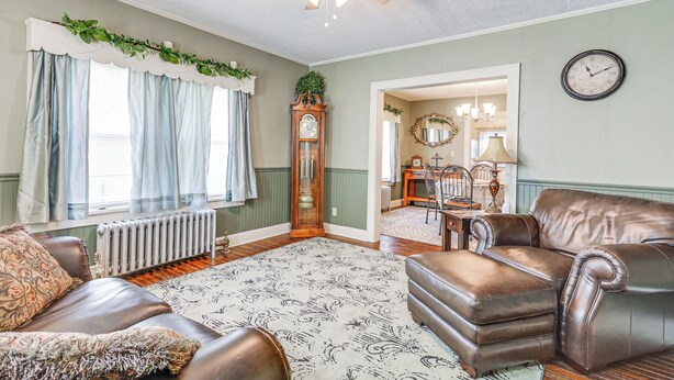 A living room with a brown leather sofa, a patterned rug, a wooden floor, a ceiling fan, and a large window with curtains. - 2 Mi to Mohegan Sun & Dtwn: Home in Norwich (Norwich)
