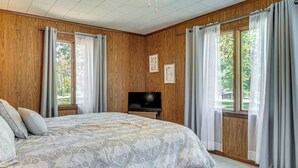 Un dormitorio con una cama grande, paneles de madera, un televisor y ventanas amplias con cortinas.