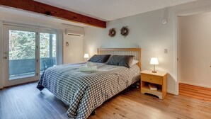 A bedroom with a large bed, wooden floor, a balcony, and a small bedside table with a lamp. - White Mtn Adventure Base! Cozy Bartlett Condo (Bartlett)