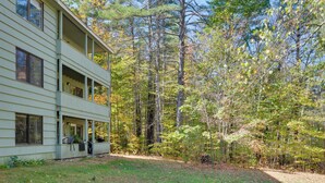 A two-story building with a covered porch and a view of a wooded area. - White Mtn Adventure Base! Cozy Bartlett Condo (Bartlett)