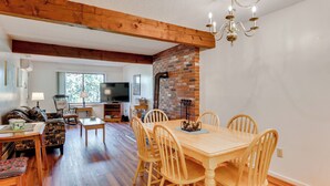 A dining area with a wooden table and chairs, a brick wall, and a chandelier. - White Mtn Adventure Base! Cozy Bartlett Condo (Bartlett)