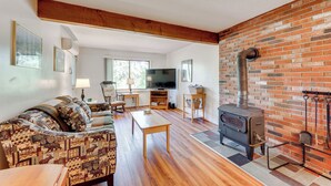A cozy living room with a sofa, a coffee table, a television, and a brick wall with a wood-burning stove. - White Mtn Adventure Base! Cozy Bartlett Condo (Bartlett)