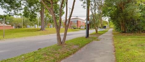 A sidewalk adjacent to a road with trees and a building in the background.