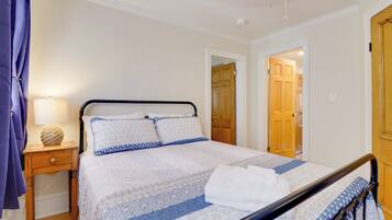 A neatly made bed with a patterned bedspread, a bedside table with a lamp, and a wooden door in the background.