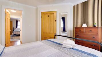 A hotel room with a bed, a wooden dresser, a mirror, and a door leading to a bathroom.