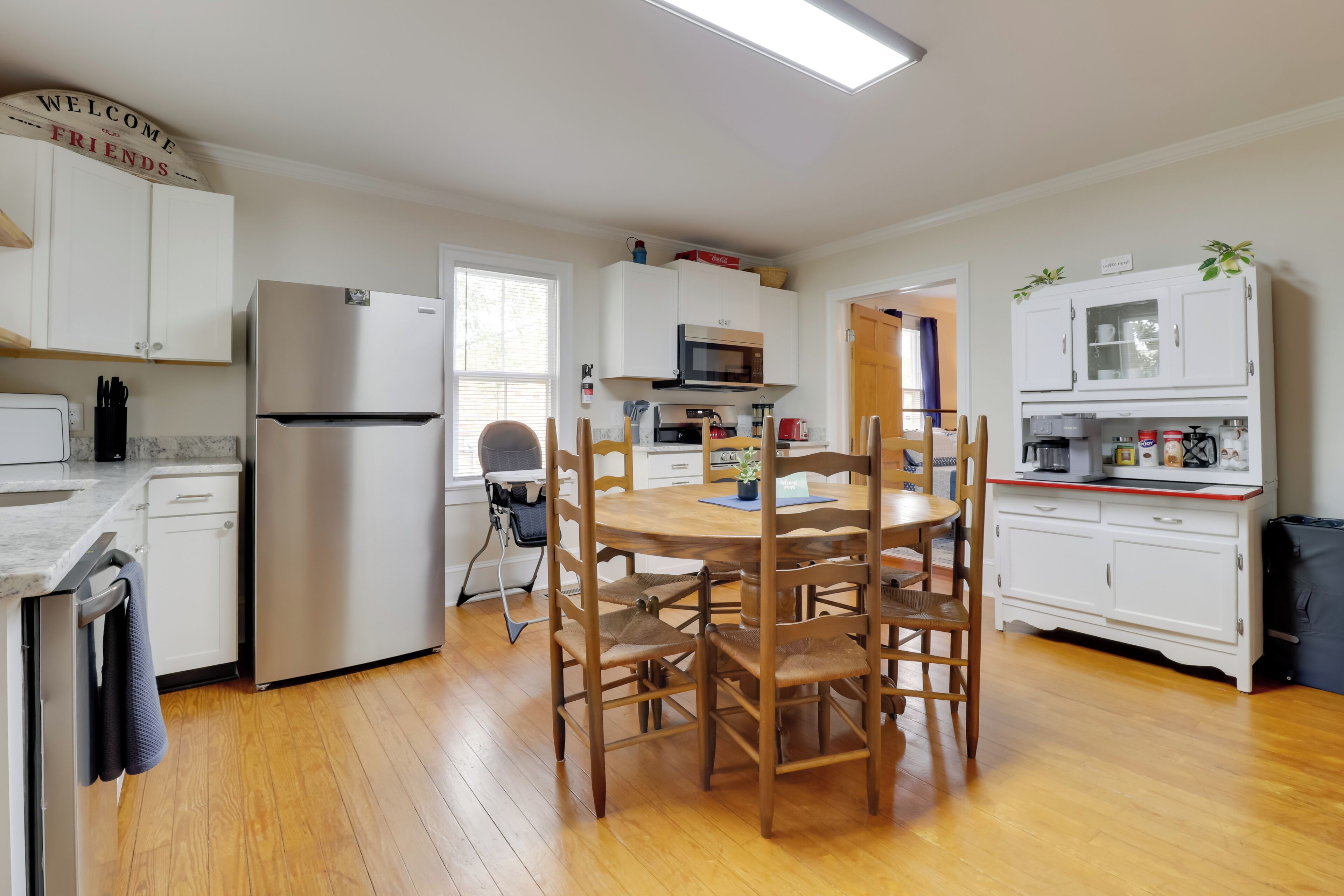 Una cocina moderna con armarios blancos, un refrigerador de acero inoxidable, una mesa de comedor de madera con sillas y un microondas.