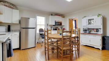 Una cocina moderna con armarios blancos, un refrigerador de acero inoxidable, una mesa de comedor de madera con sillas y un microondas.