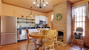 A kitchen with a brick fireplace, wooden dining table, and chairs, and a high chair. - Walk to Downtown: Historic Home in Edentons Heart (Edenton)