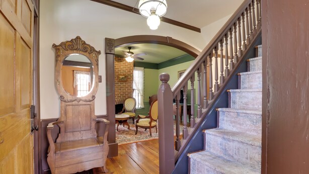 A wooden staircase with a handrail, a round mirror, and a wooden bench in a room with a brick wall and a ceiling fan. - Walk to Downtown: Historic Home in Edentons Heart (Edenton)