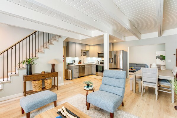 A spacious living area with a staircase, a dining table, and a kitchen in the background.