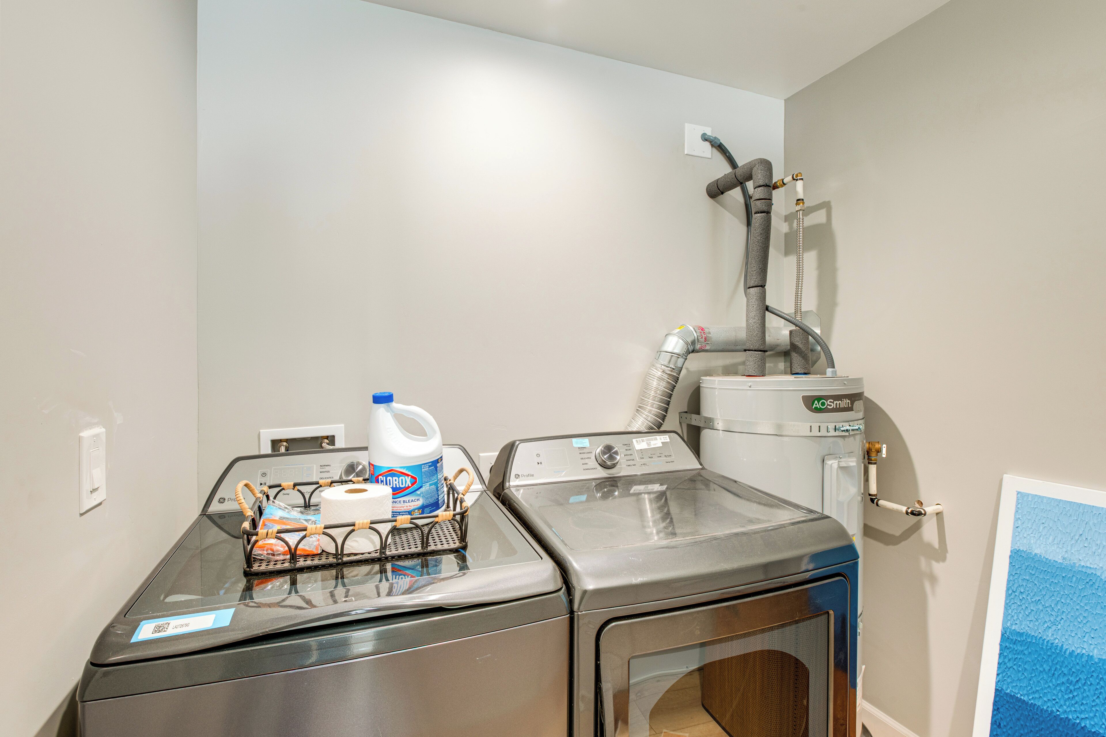 A laundry room with two washing machines, a water heater, and a hose.