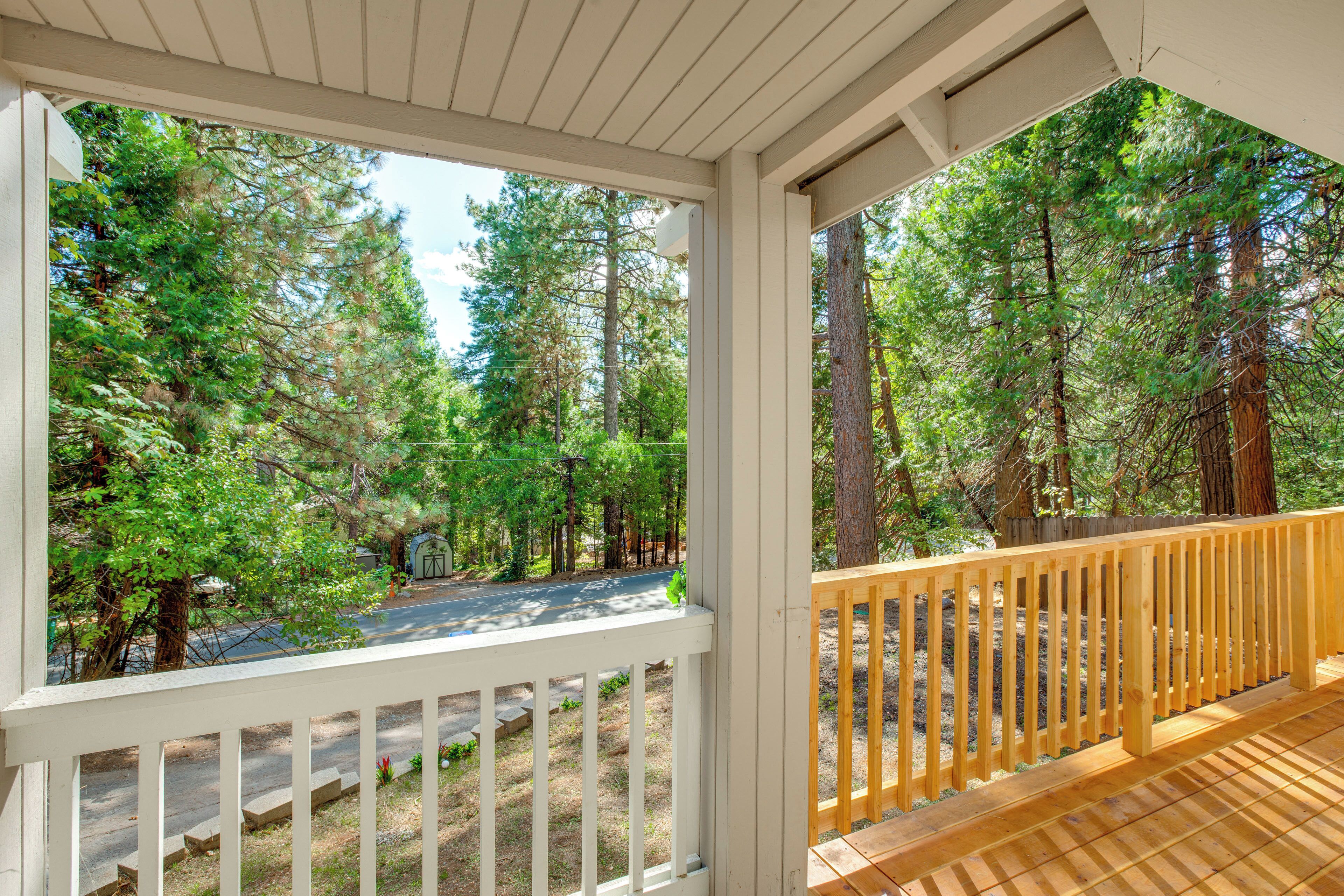 A wooden deck with a white railing overlooking a forested area with a road.