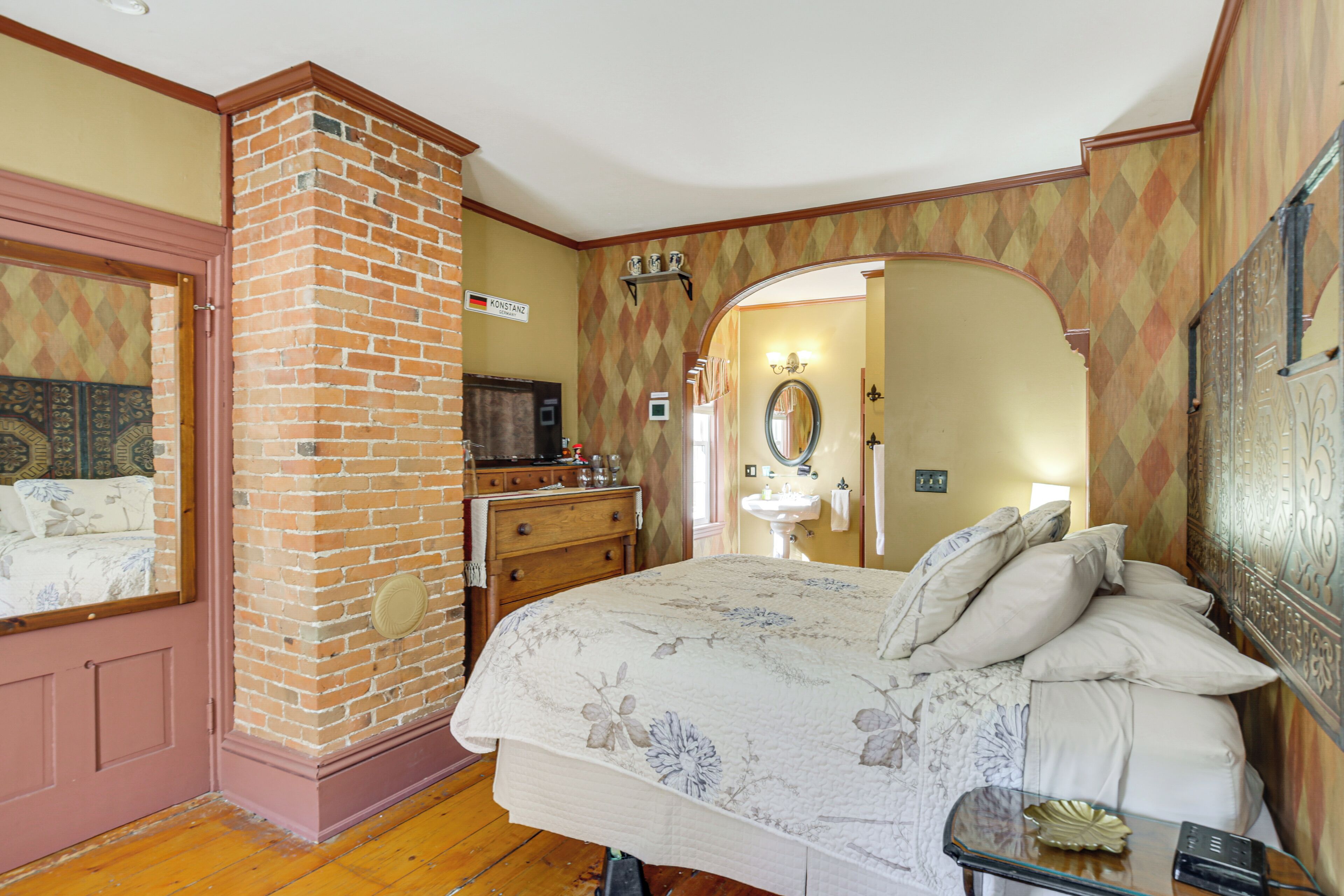 Un dormitorio con chimenea de ladrillo, una cama con ropa de cama floral, un aparador y un tocador con espejo.
