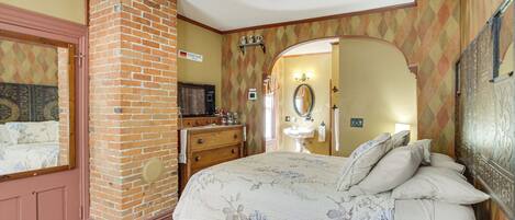 Un dormitorio con chimenea de ladrillo, una cama con ropa de cama floral, un aparador y un tocador con espejo.