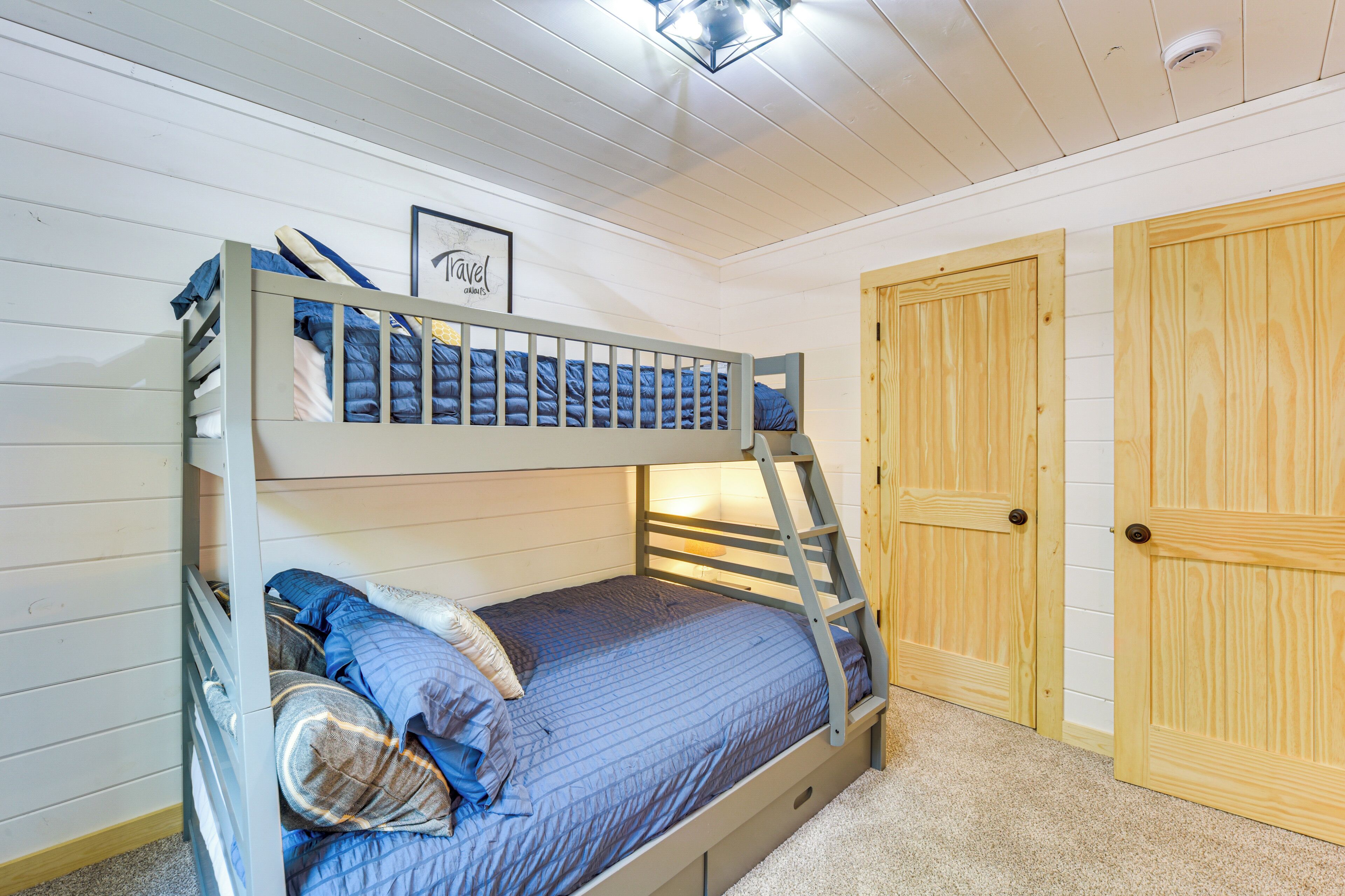 Een stapelbed met een ladder, een ingelijst plaatje aan de muur en houten deuren.