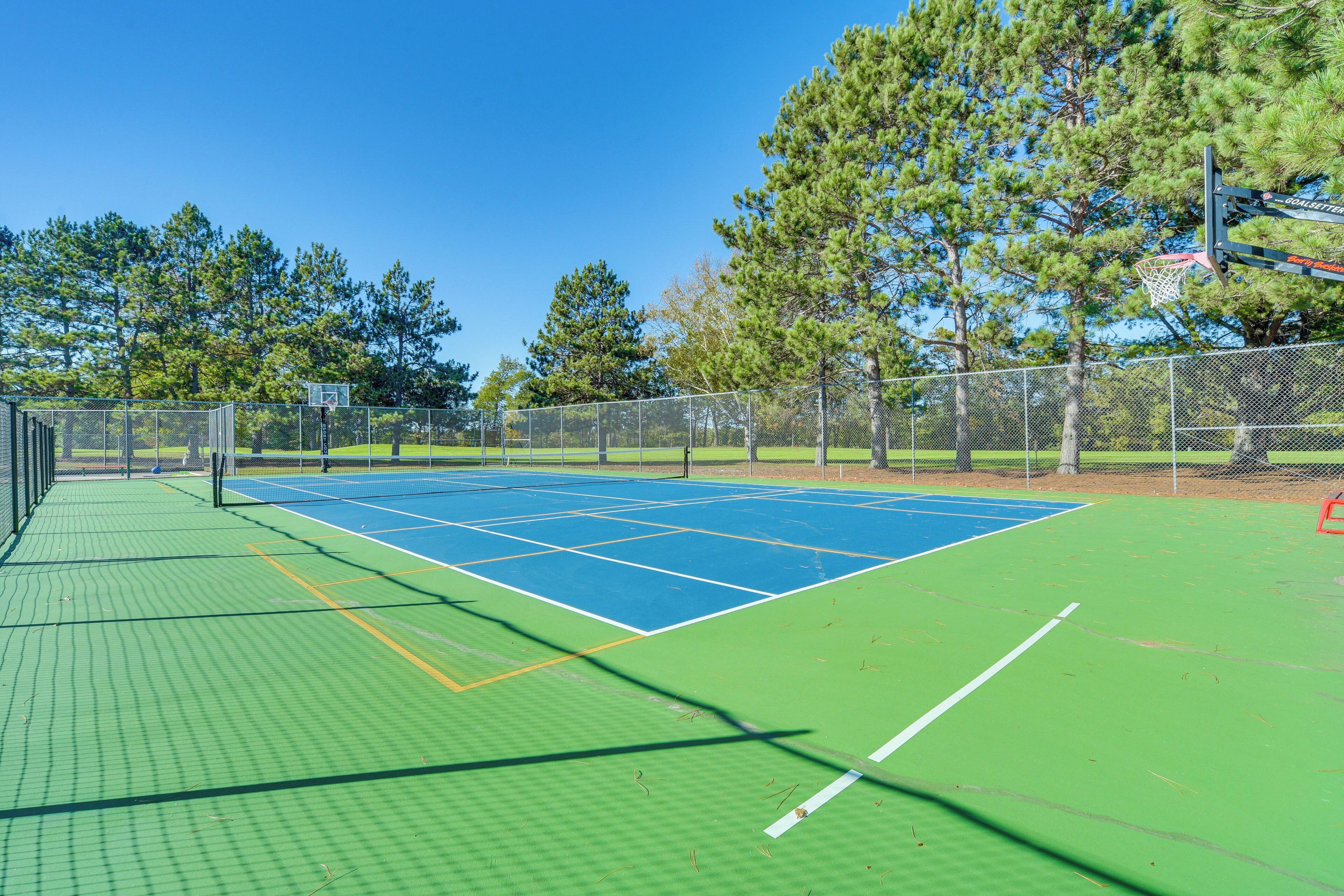 A tennis court with a net, surrounded by a fence and trees.