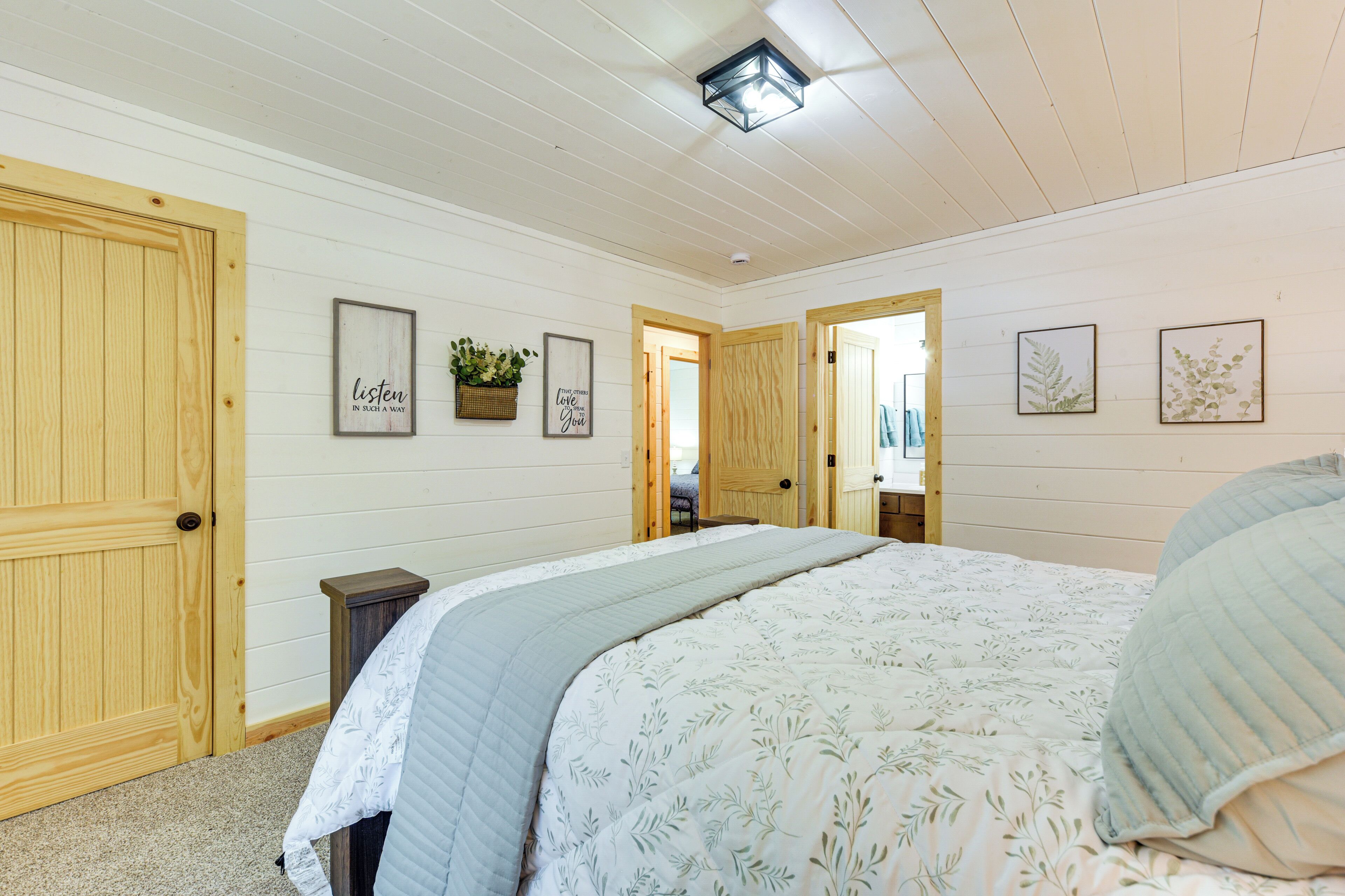A bedroom with a large bed, wooden doors, and framed wall art.