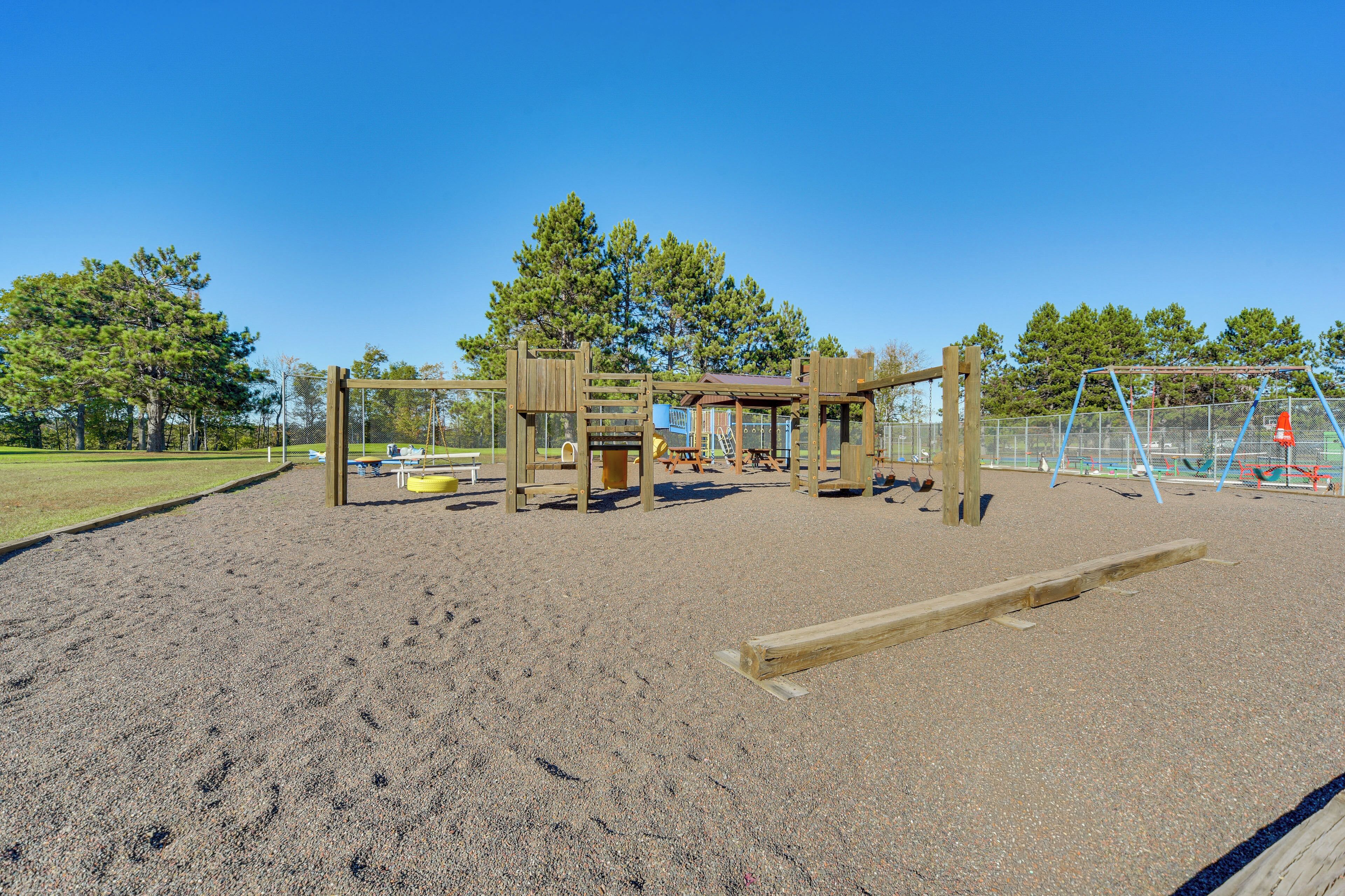 A playground with a wooden play structure, a sandpit, and a fenced area.