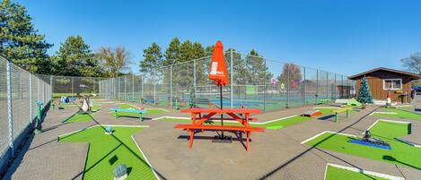 A playground with a red picnic table, green artificial grass, and a fenced area.