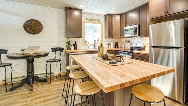 Eine moderne Küche mit Holzschränken, einem Edelstahlkühlschrank, einer Mikrowelle und einer Holzinsel mit Hockern.