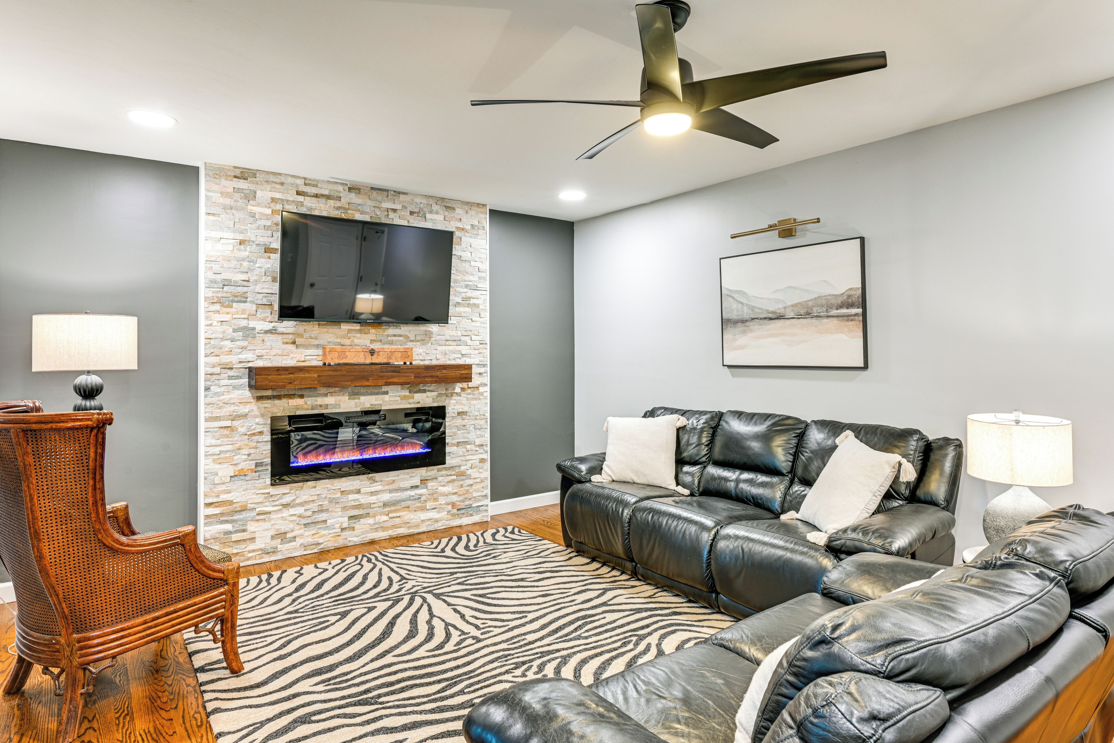 A modern living room with a stone fireplace, leather sofa, and a zebra-patterned rug.