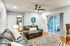 Ein Wohnzimmer mit einer Ledersofa, einem Zebra-Teppich, einem Deckenventilator und einer Glastür, die zu einem Außenbereich führt.