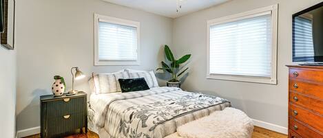 A bedroom with a bed, a nightstand, a dresser, a ceiling fan, and two windows with blinds.