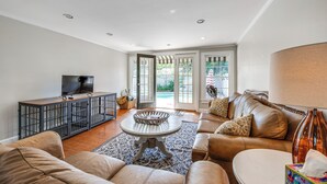 A spacious living room with a leather sofa, a coffee table, and a TV on a wooden console. - Walk to Dtwn Hahira: Inviting Home w/ Pool & Yard! (Hahira)