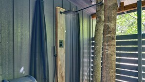 A wooden cabin with a shower area, a trash bin, and a wooden deck.