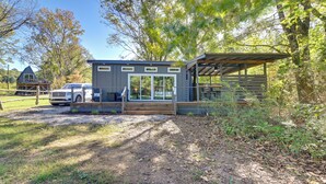 A modern cabin with a covered porch, a vehicle parked in front, and a natural, wooded setting.
