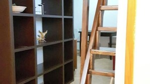 A room with a wooden staircase, a dark-colored shelving unit with a bowl and a small statue, and a tiled floor. - The Relaxation Den (Palestrina)