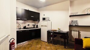 A compact kitchen with dark cabinets, a white refrigerator, and a dining area with two chairs. - The Relaxation Den (Palestrina)