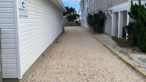 A narrow gravel pathway between two buildings with white siding, a visible number '226', and a sign for Carolina Beach Real Estate. - Turtle Cove - Cozy retreat steps from the ocean, (Kure Beach)