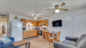 A modern kitchen with wooden cabinets, a dining area with a table and chairs, and two ceiling fans. - Turtle Cove - Cozy retreat steps from the ocean, (Kure Beach)