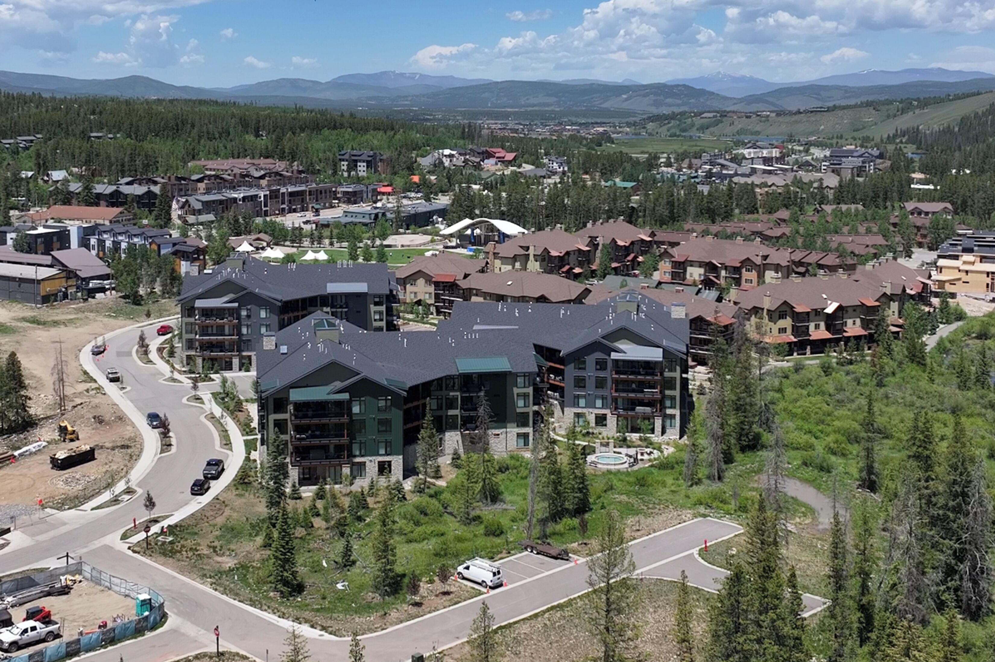 A modern hotel complex with multiple buildings, a parking area, and a view of surrounding mountains.