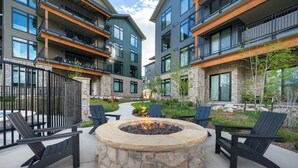 Un cortile con un braciere in pietra circondato da poltrone Adirondack, edifici moderni a più piani e un sentiero in pietra.