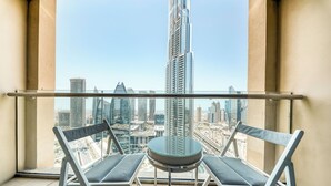 A balcony with two chairs and a small table, offering a view of a cityscape with modern skyscrapers. - PVH - Emaar Residences - Studio (Dubai)