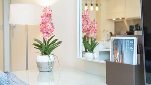 A modern interior with a white table, a potted orchid, and a magazine rack with a 'TOP' magazine. - PVH - Emaar Residences - Studio (Dubai)