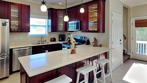 Une cuisine moderne avec des meubles de couleur bois foncé, un grand îlot central doté de tabourets, des appareils électroménagers en acier inoxydable et un éclairage suspendu.
