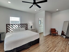 Une chambre à coucher comprenant un lit, une table de chevet, une chaise, un miroir et un ventilateur de plafond.