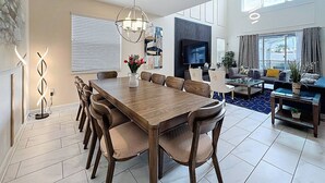 A spacious living area with a large wooden dining table, comfortable seating, a flat-screen TV, and a cozy seating area with cushions and a coffee table. - Luxe & Leisure Lodge: Free Resort Access! (Davenport)