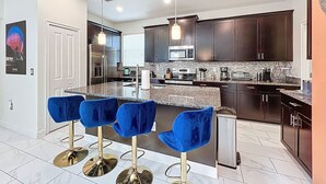 A modern kitchen with dark cabinets, a granite countertop, and a central island with bar stools. - Luxe & Leisure Lodge: Free Resort Access! (Davenport)