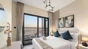 A hotel room with a large bed, a desk, a chair, a balcony with a view, and artwork on the walls.