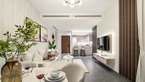 A modern living room with a dining area, a kitchen in the background, and a TV mounted on the wall.